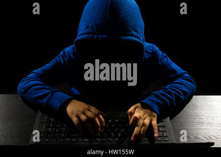 Faceless hacker with laptop in black isolated background. Stock Photo