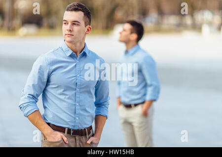 Two businessman standing outdoor one is holding a phone and looking at camera with blur background city Stock Photo