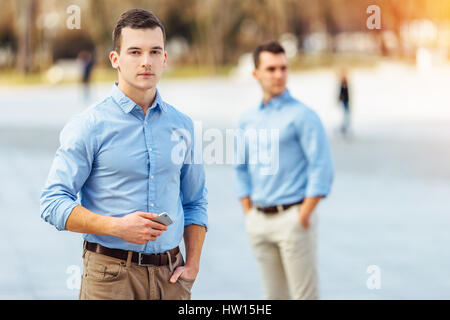 Two businessman standing outdoor one is holding a phone and looking at camera with blur background city Stock Photo