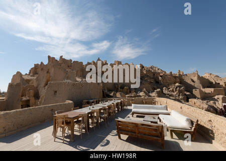 Traditional old Arabian heritage house lodge  rooftop with wood dinning tables and chairs  with background view of old city walls in siwa oasis egypt