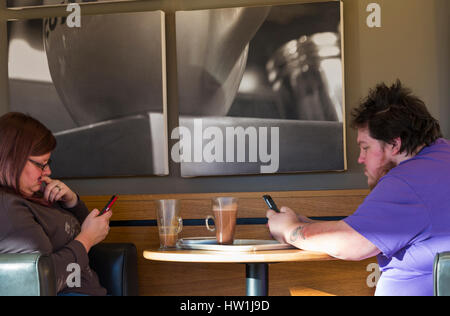 Man and woman sitting at table with a glass of latte drink while looking at mobile phones in cafe Stock Photo