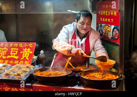 WANGFUJING NIGHT MARKET, BEIJING - DEC 25, 2013 - A vendor serves spicy Korean rice cakes at Wangfujing snack street, Beijing. Stock Photo