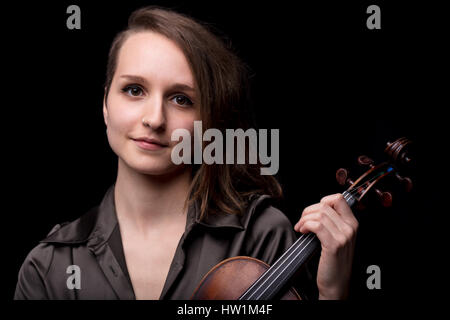 portrait of a young violinits woman holding her violin headstock with a slight smile, concept of classical music Stock Photo