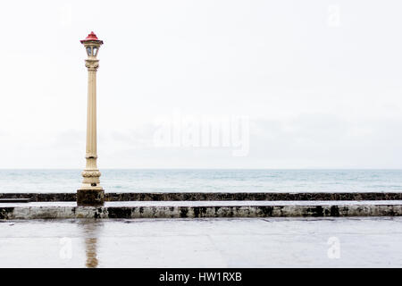 A victorian retro lamp post and road side curb and path at the sea side beach front on an overcast rainy day. Stock Photo