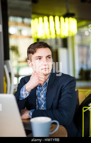 Male freelancer connecting to wireless via laptop computer, thoughtful businessman work on net-book while sitting at wooden table in modern coffee sho Stock Photo
