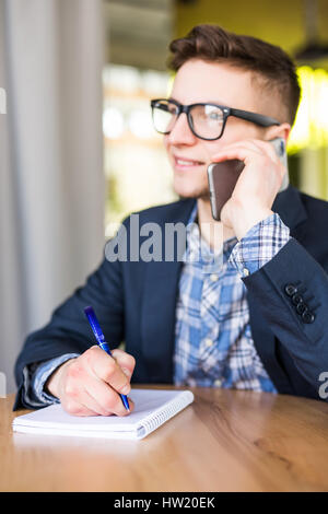 Freelance man make notes in notebook and talking by phone in office Stock Photo