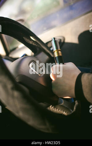 young vaper man with beard vaping mechanical mod. Guy smokes an electronic cigarette by blowing a smoke vapor. Holds in hand Sitting at the wheel of a Stock Photo