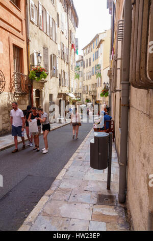 Tourists and locals on a charming street in Grasse, Provence, France. Tall buildings offer shade from hot sun in this town nestled in the French Alps. Stock Photo