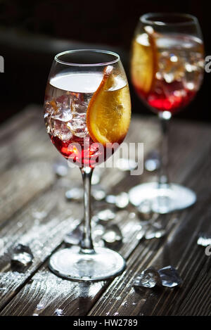 Two refreshing red cocktails with orange isolated on a wooden background with oranges and ice with backlight Stock Photo