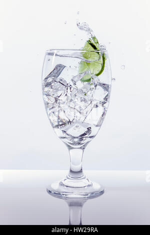 A lime sliced makes a splash after being dropped into a glass of ice water. Stock Photo