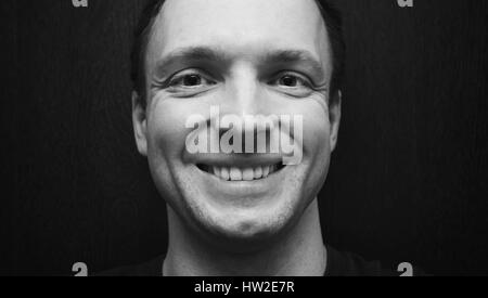 Young handsome smiling Caucasian man. Close-up studio face portrait over dark wooden wall background, selective focus, black and white photo Stock Photo