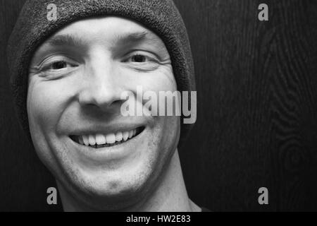 Young handsome smiling man in gray hat. Closeup studio face portrait over dark wooden wall background, selective focus, black and white photo Stock Photo