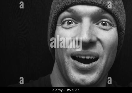 Young handsome smiling man in gray hat. Low key studio face portrait over dark wooden wall background, selective focus, black and white photo Stock Photo