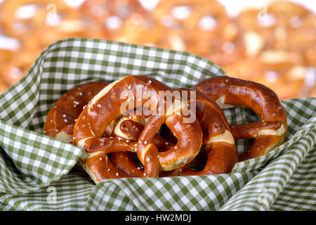 Fresh handmade original Bavarian pretzels from the domestic master baker on a green checkered tea towel; many blurry pretzels in the background Stock Photo