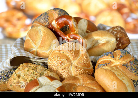 Various fresh Bavarian rolls and pretzels from the domestic master baker on a checkered tea towel; many blurry bakery goods in the background Stock Photo