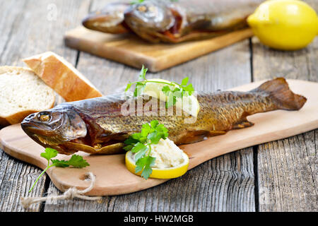 A smoked rainbow trout served on a wooden cutting board with horseradish, parsley, lemon  and baguette Stock Photo