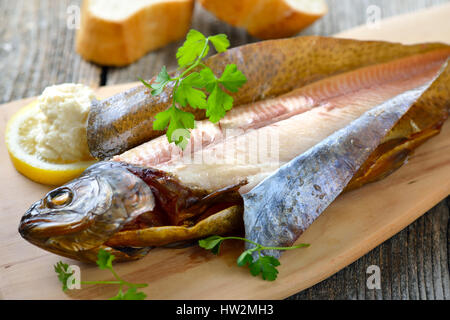 A smoked rainbow trout served on a wooden cutting board with horseradish, parsley, lemon  and baguette Stock Photo