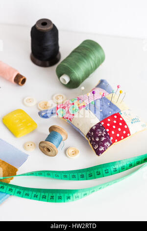 set concept for sewing. production of patchwork quilt. measure tape, color bobbin of thread, pin cushion with sewing pins, buttons and fabric pieces on a white background. tool kit of the tailor. Stock Photo