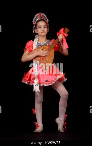 Cute little girl wearing native russian costume isolated on black background. She is dancing and holding balalaika in hands Stock Photo