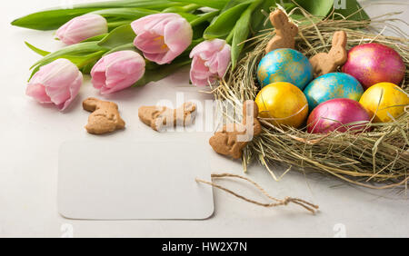 Easter eggs in a straw nest, Easter bunny cookies and tender pink tulips lie on the background of a white table Stock Photo