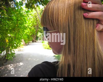 Closeup of a beautiful girl, young woman wearing sunglasses, looking away holding hand on her head showing  nail design. Exotic island,green vegetatio Stock Photo