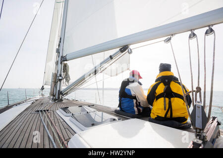Rear view of people wearing waterproof jackets sitting on yacht deck in sea Stock Photo