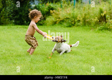 Happy boy playing with dog active game on lawn Stock Photo