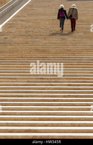 Two older people walking hand in hand together up the stone steps of the Renzo Piano designed entrance and parliament building at the City of Valetta  Stock Photo