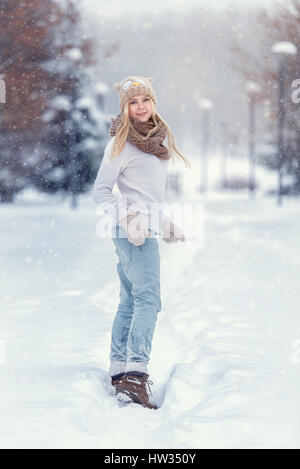 Attractive young blonde girl walking in winter forest. Pretty woman in wintertime outdoor. Wearing winter clothes. Knitted sweater, scarf, hat and mit Stock Photo