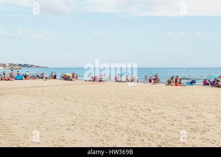 A beautiful summer day at a beach with lots of people with colorful swimsuits sunbathing and enjoying the hot sun. Stock Photo
