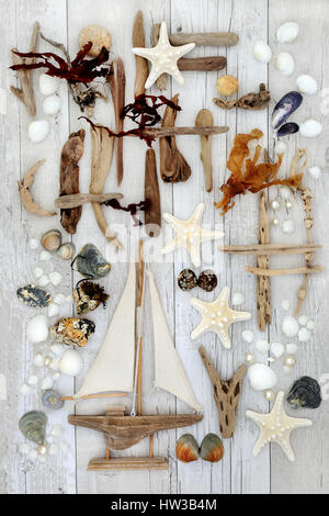 Abstract seaside collage with decorative sailing boat, driftwood, seashells, rocks, pearls and seaweed on distressed white wood background. Stock Photo