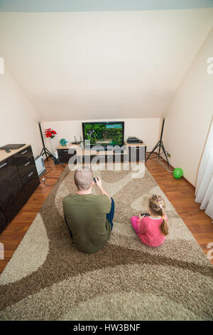 father and daughter sit on the floor and playing on the console Stock Photo
