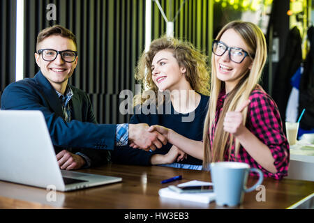 Young freelancers are using gadgets, talking and smiling while working at the modern office. Men are handshaking Stock Photo