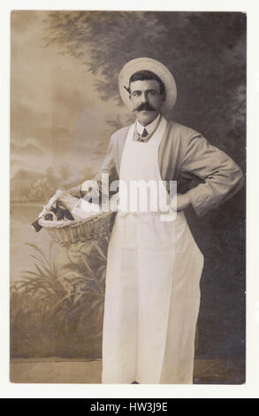 Edwardian postcard of Grocer shop owner, staff or assistant, carrying his basket of groceries, studio portrait, U.K  circa. 1910 Stock Photo