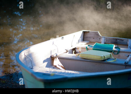 Old fishing boat moored on the sand with the morning sun streaming on it and fog rolling off the water. Stock Photo