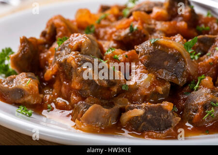 Close up of chicken gizzard stew on plate with herbs on wooden rustic background Stock Photo