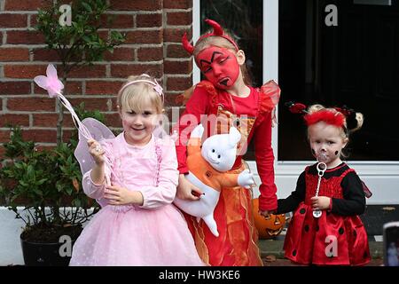 three girls children wearing fairy, devil and ladybird costumes dressed up at Halloween, family in fancy dress Stock Photo