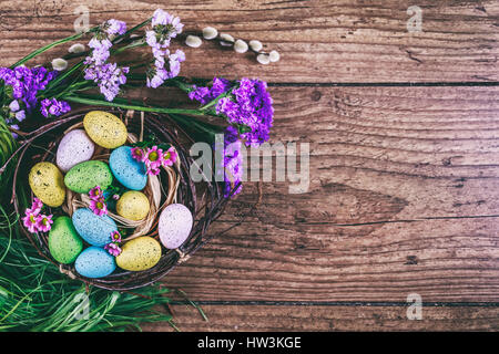 Happy Easter. Easter background. Bright colorful eggs in nest with spring flowers over wooden dark background. Selective focus with copy space. Stock Photo