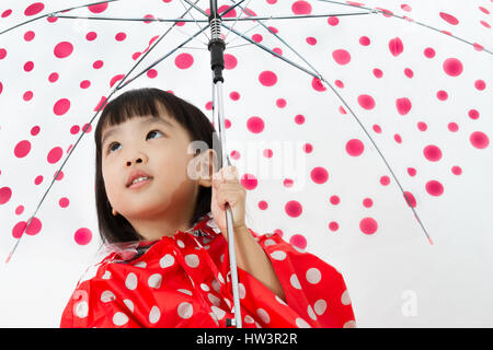 Chinese Little Girl Holding umbrella with raincoat in plain white isolated background. Stock Photo