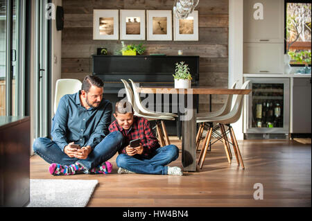 Smiling father and son sitting on floor texting on cell phones Stock Photo