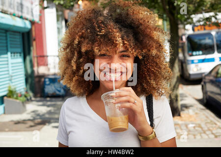 Black woman drinking with straw on city sidewalk Stock Photo