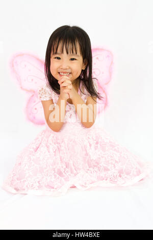Chinese little girl wearing butterfly custome with praying gesture in plain white background Stock Photo
