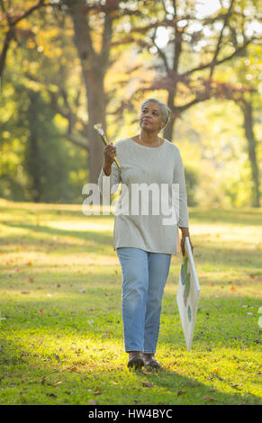 Pensive Black woman carrying paintbrushes and canvas in park Stock Photo