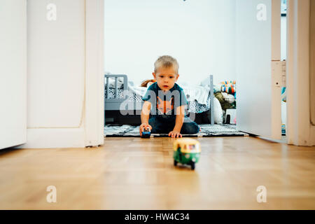 Boy kneeling on floor pushing toy cars Stock Photo