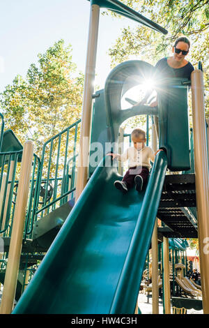 Mother watching son on playground slide Stock Photo