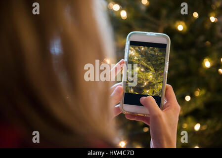 Caucasian woman photographing Christmas tree with cell phone Stock Photo