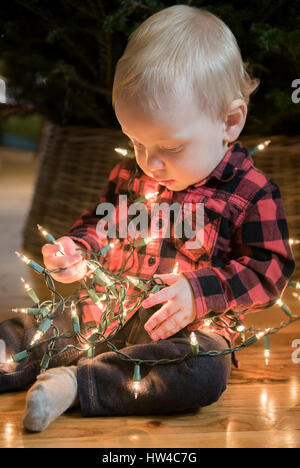 Caucasian baby boy sitting on floor wrapped in string lights Stock Photo