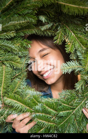 Mixed Race woman winking in pine wreath Stock Photo