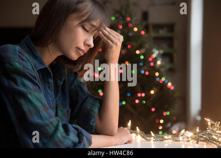 Mixed Race woman with headache near Christmas tree Stock Photo
