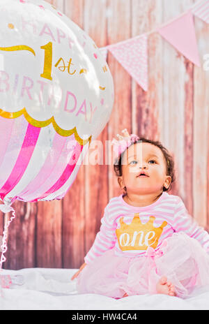 Mixed Race baby girl sitting near birthday balloon Stock Photo